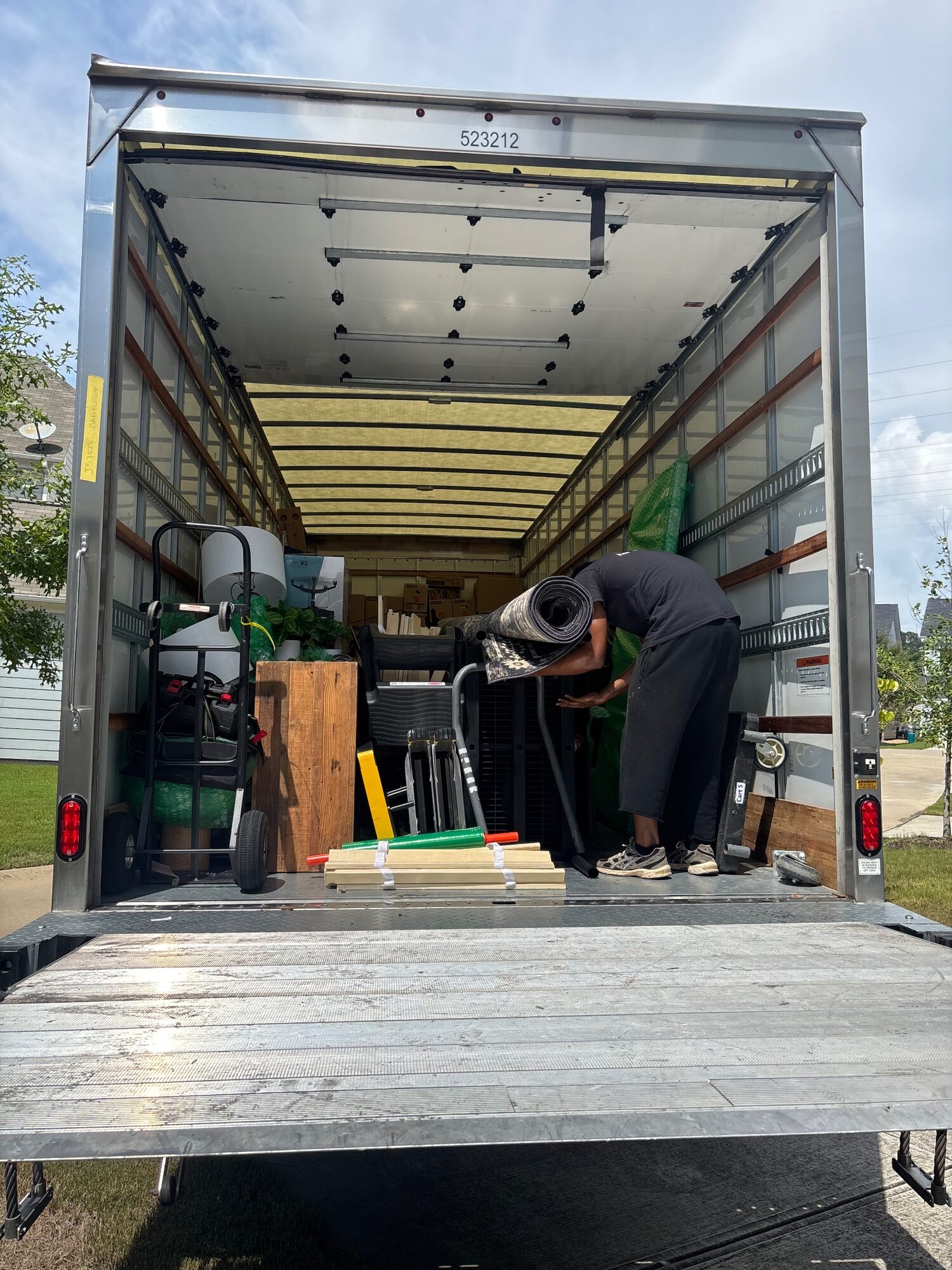 Clays Moving crew member lifting a rolled rug into a loaded box truck